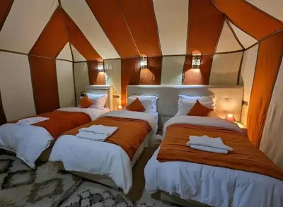 a room with three beds with orange and white sheets at Merzouga sands camp in Merzouga
