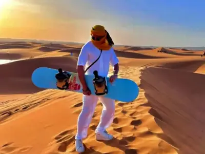 a man standing in the desert holding a snowboard at Luxury Dune's Camp in Merzouga