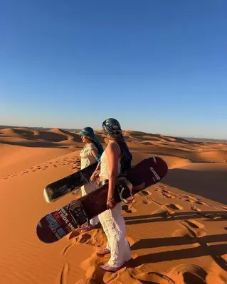 two people are standing in the desert with snowboards at Tilila Luxury Camp in Merzouga