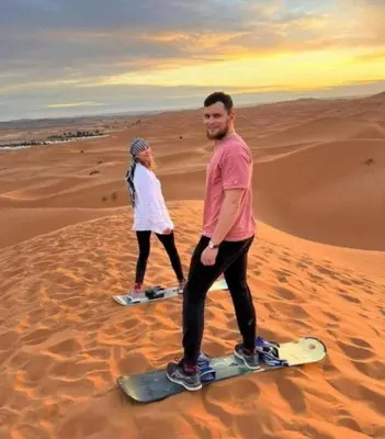 two people standing on snowboards in the desert at Tilila Luxury Camp in Merzouga