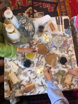 a table with a table cloth with food and a child holding a spoon at le sirwa salam in Anzel
