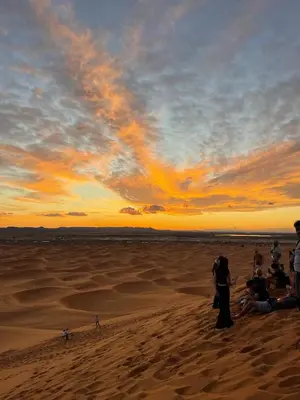 a group of people sitting on the beach at sunset at Fabulous Luxury Camp in Merzouga