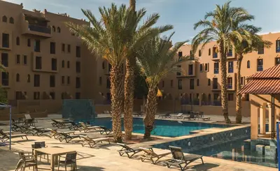 a resort pool with chairs and palm trees and buildings at Hôtel Reda Zagora in Zagora