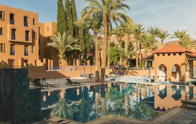 a pool at a resort with palm trees and buildings at Hôtel Reda Zagora in Zagora