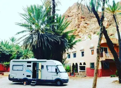 a white caravan parked in front of a building with palm trees at Le LAC Auberge Camping Todra in Tinerhir