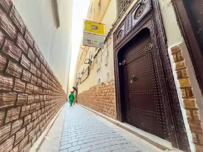 a person walking down a narrow alley with a large door at vintage in Fès