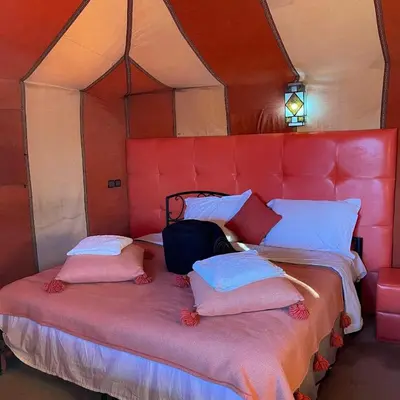 a bed in a room with a red head board at Unique Sahara Camp in Merzouga