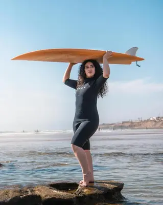 a woman standing on a rock holding a surfboard at Tayyurt Blue waves Beach house's in Oulad Akkou