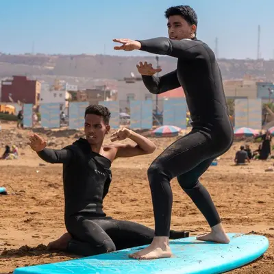 two men sitting on surfboards on a beach at Tayyurt Blue waves Beach house's in Oulad Akkou