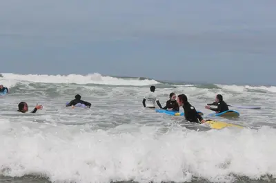 a group of people sitting on surfboards in the ocean at Tayyurt Blue waves Beach house's in Oulad Akkou