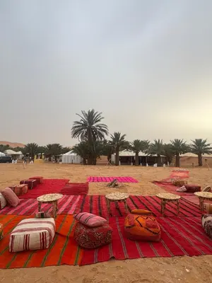 a blanket with tables and pillows on a beach at Sahara Experience Luxury Camp in Merzouga