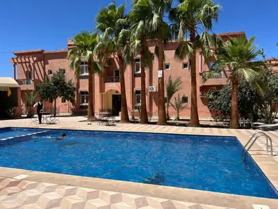 a swimming pool in front of a building with palm trees at COMPLEXE TOURISTIQUE ARTIZANAL bab sahara in Oulad Akkou