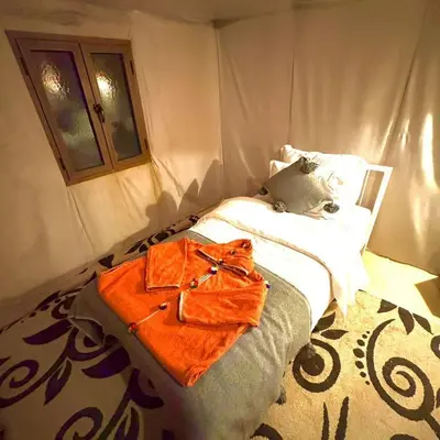 a bedroom with a bed with an orange bag on it at irrigation desert camp in Merzouga