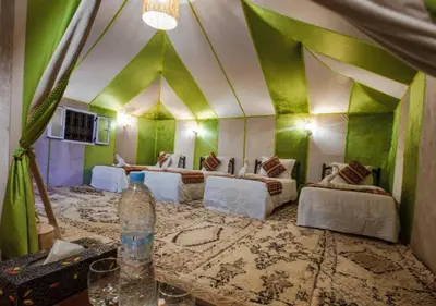 a room with four beds and a bottle of water on a table at Slik Sand Oasis Camp in Merzouga