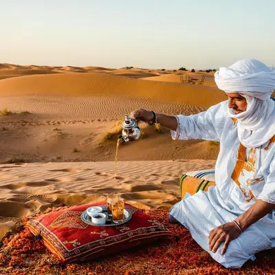 a man sitting in the desert with a plate of food at Under 1000 Stars Camp in Merzouga