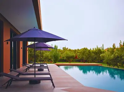 a group of chairs with umbrellas next to a swimming pool at Villa Timenkar - Moroccan spa and mountain panorama in Aghmat