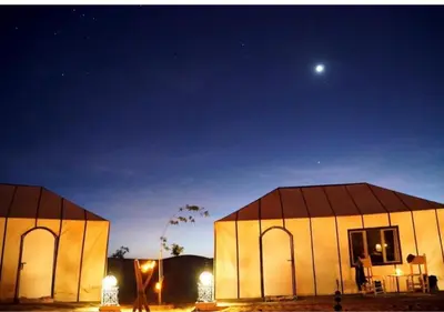 two domed buildings at night with the moon in the sky at Sahara Whisper Luxury Camp in Merzouga