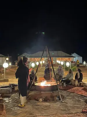 a group of people sitting around a fire at night at Peaceful Luxury Camp in Merzouga