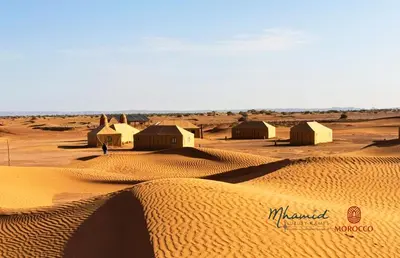 a desert with a group of huts in the sand at mhamid luxury camps in Mhamid El Ghizlane