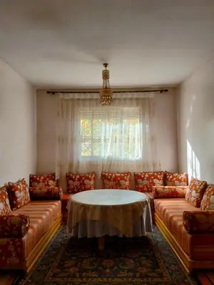 a living room with couches and a table and a window at Ravissante appartement dans les jardins in Oulad Akkou