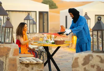 a woman serving a woman at a table at sahara bliss camp in Merzouga