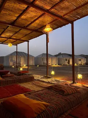 a row of mattresses under a wooden structure with lights at farah desert camp in Kasr Bounou