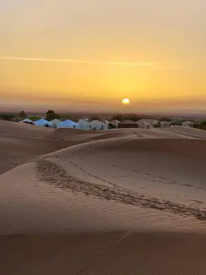 a sunset in the desert with footprints in the sand at Desert Live Luxury Camp in Merzouga