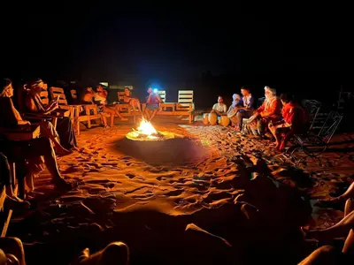 a group of people sitting around a fire on the beach at Oasis Desert Luxury Camp in Merzouga