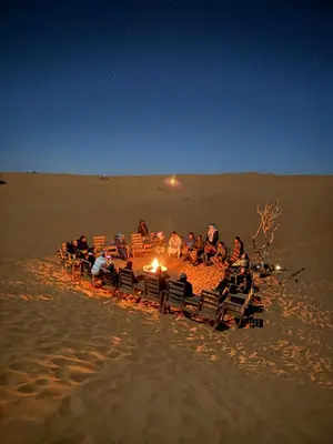 a group of people sitting around a fire on the beach at Oasis Desert Luxury Camp in Merzouga