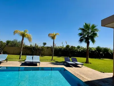 two lounge chairs and a swimming pool with palm trees at Villa de luxe à louer à la journée A Marrakech in Marrakech