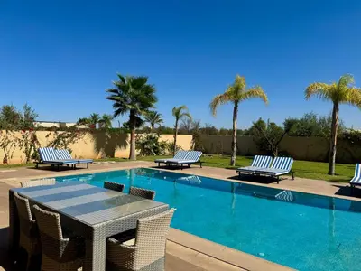 a swimming pool with chairs and a table and palm trees at Villa de luxe à louer à la journée A Marrakech in Marrakech