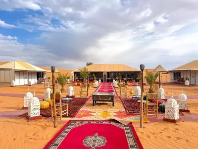 a compound with tables and chairs and a red carpet at Desert Pearl Camp Merzouga in Merzouga
