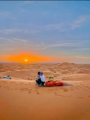 two people sitting in the desert watching the sunset at Nights luxury camp in Merzouga