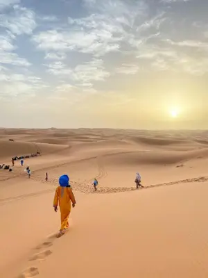 a group of people walking through the desert at moroccan izem camp in Merzouga