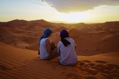 two people sitting in the desert watching the sunset at moroccan izem camp in Merzouga