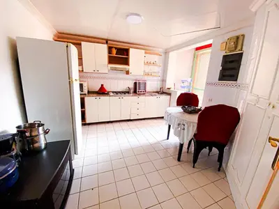 a kitchen with a table and red chairs and a table and a refrigerator at Appartement d'orient centre ville in Oulad Akkou