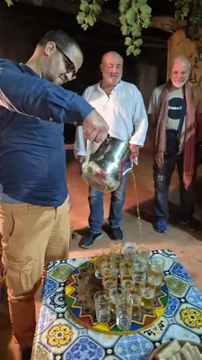 a man holding a pot in front of a table with glasses at Dartagounite in Oulad Akkou