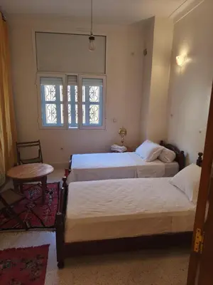 a bedroom with two beds and a table and a window at maison de tourisme el amal in Oulad Akkou