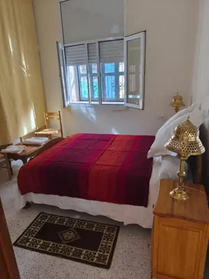 a bedroom with a bed with a red blanket and a window at maison de tourisme el amal in Oulad Akkou