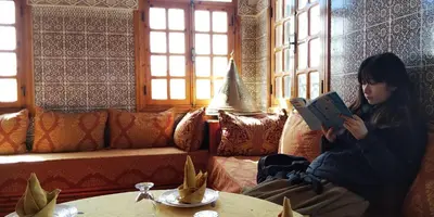 a woman sitting on a couch reading a book at hotel and restaurant kasbah draa in Agdz