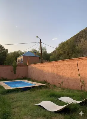 a swimming pool in the grass next to a wall at Villa d'Exception à Ourika Nichée au Cœur des Montagnes in Aghbalou