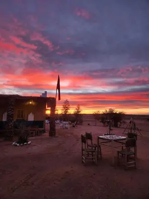 a sunset with a table and chairs in the desert at Camping Meteorite in Merzane