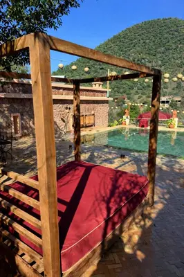 a wooden canopy bed in front of a swimming pool at villa lalla Ourika & heated pool in Oulad Akkou