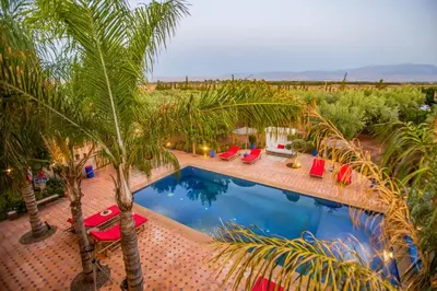 a swimming pool with red chairs and palm trees at Domaine avec gouvernante 5 chambres, piscine, hamam et ferme pédagogique sur un hectare in Had Abdallah Rhiat