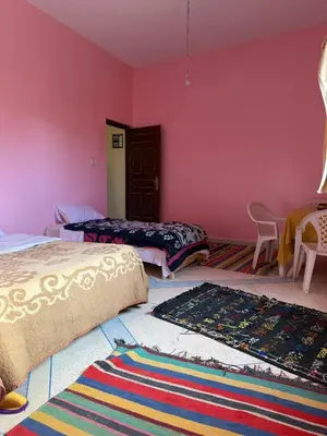a bedroom with two beds and a rug on the floor at Maison La Baraka Merzouga in Merzouga