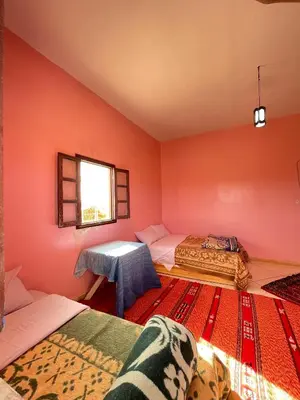 a room with two beds and a table in it at Maison La Baraka Merzouga in Merzouga