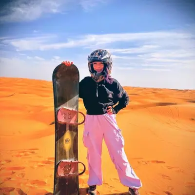 a person standing in the desert with a snowboard at Merzouga Hero luxury Glamping in Merzouga