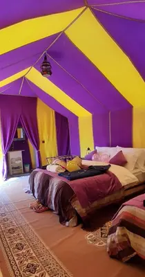 a purple and yellow tent with two beds in it at Sahara Waves Luxury Camp in Merzouga