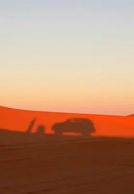 a shadow of a car in the desert at sunset at Sahara Waves Luxury Camp in Merzouga