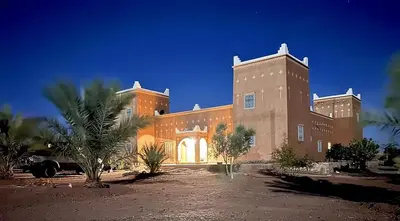 a large brick building with palm trees in front of it at Guest house Kasbah Foum Tizza in Boikhlal